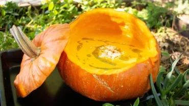 Soupe décorée avec de l’huile verte et des amandes concassées présentée dans sa courge