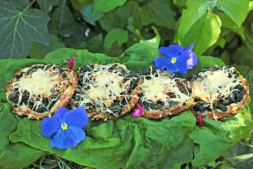 Les tartelettes sont installées au potager sur des feuilles d'épinard et quelques fleurs comestibles déposées autour : capucine et sauge