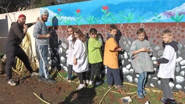 un groupe d'enfants et deux animateurs peignent des fleurs sur un mur