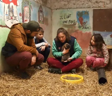 Deux enfants et deux adultes sont dans un enclos avec un lapin dans les bras