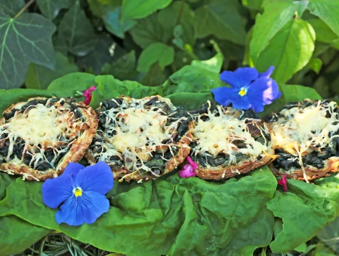 Les tartelettes sont installées au potager sur des feuilles d'épinard et quelques fleurs comestibles déposées autour : capucine et sauge