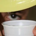 Une goutte d'eau coule d'une assiette avec un verre en dessous et l'œil d'un enfant derrière